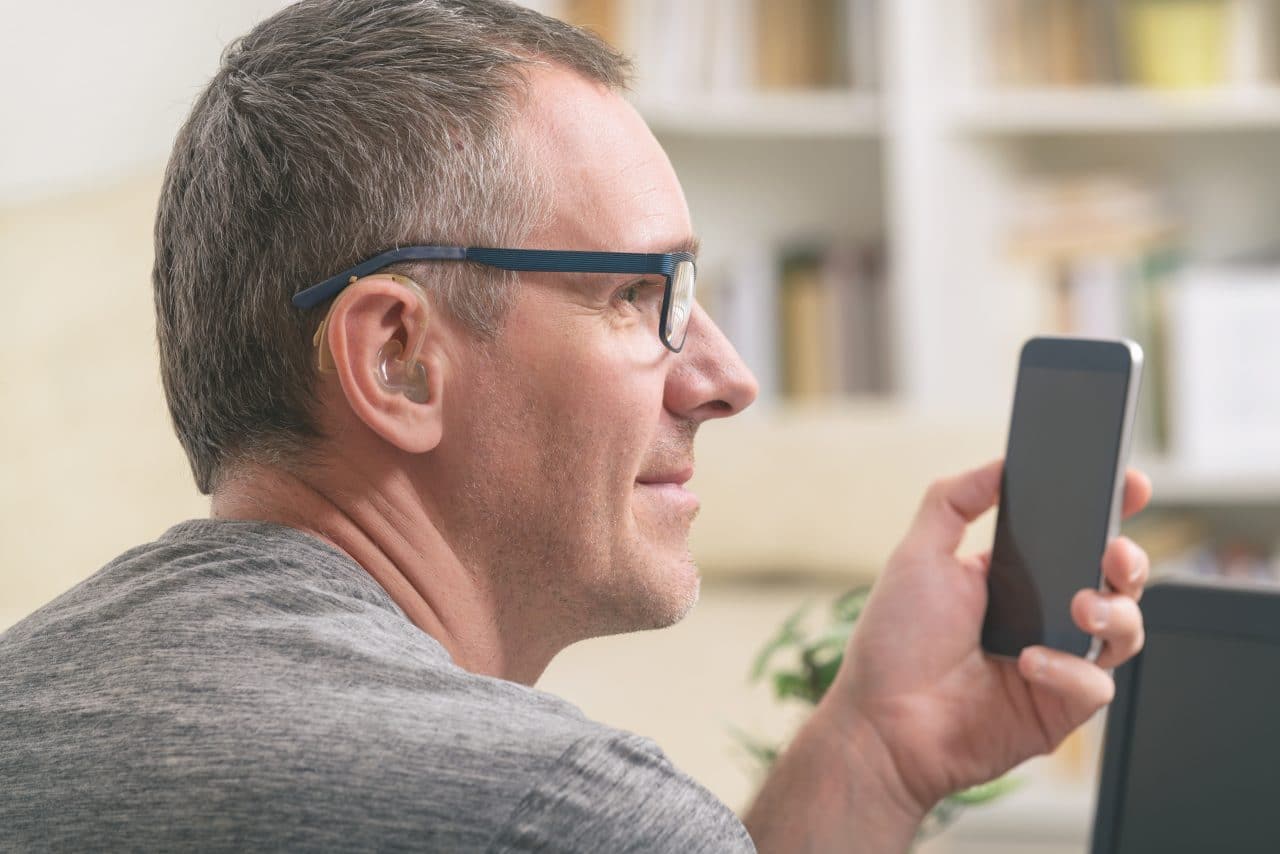 Man with hearing aid uses his phone.