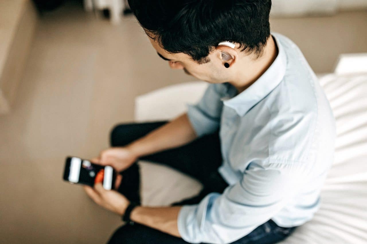 Younger man wearing a hearing aid using a smartphone.