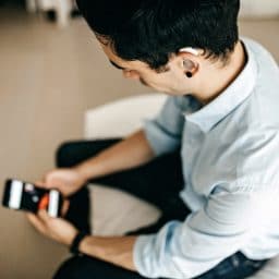 Younger man wearing a hearing aid using a smartphone.