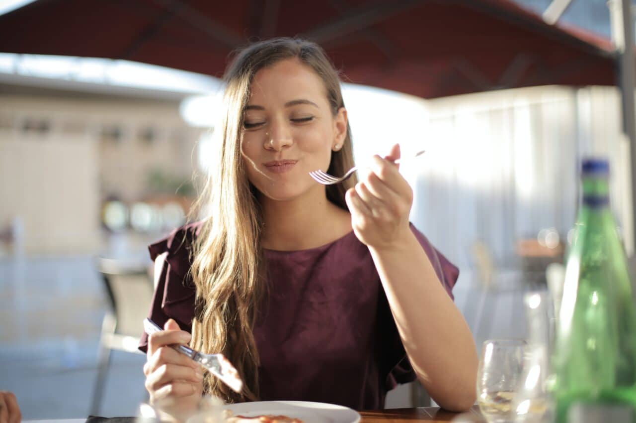 Woman enjoying a bite of food at an outdoor restaurant.