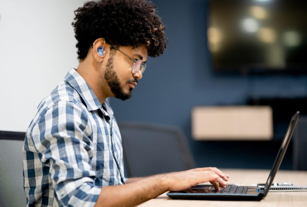 Side view of hearing impaired man working on laptop at office