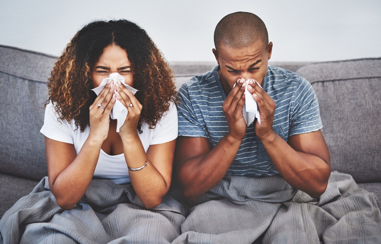 A couple blowing their noses on the couch.